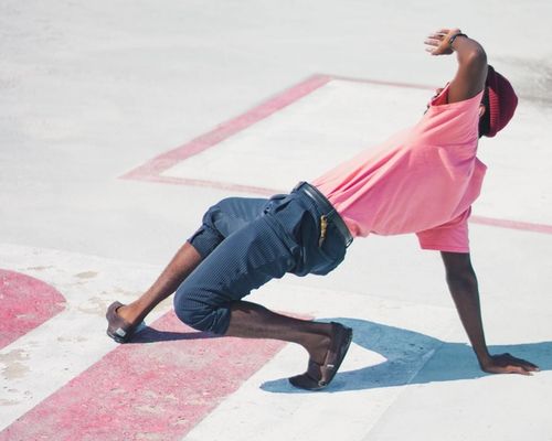 Une danseuse de rue portant un t-shirt rose et un pantalon bleu exerce une figure au sol.
