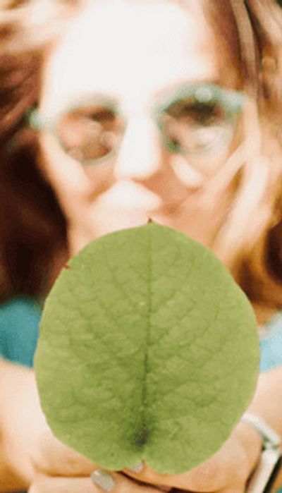 Frau mit Brille hält ein grünes Blatt in ihren Händen und streckt die Arme nach vorne.