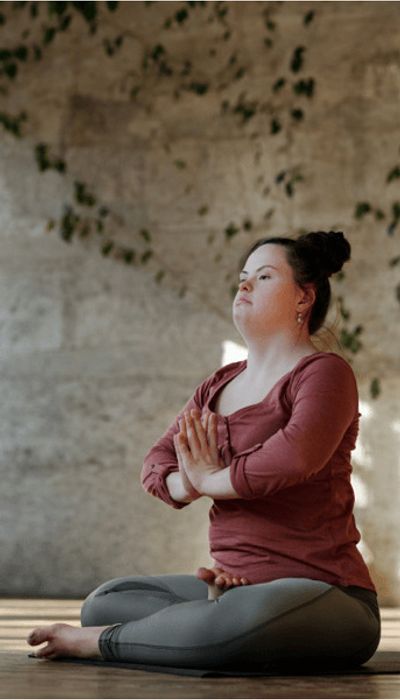 Une femme atteinte du syndrome de Down est assise sur le sol en position de yoga, les paumes tournées vers sa poitrine