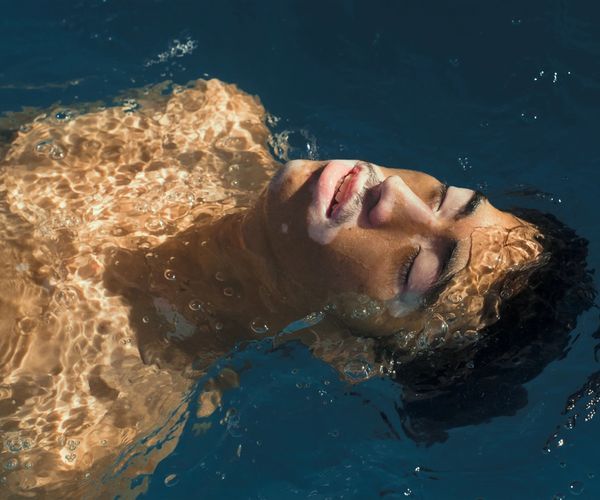 Un homme est allongé sur le dos dans une piscine avec le soleil qui brille sur son visage.