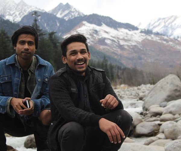Deux hommes accroupis près d'une rivière souriant au pied d'une montagne.