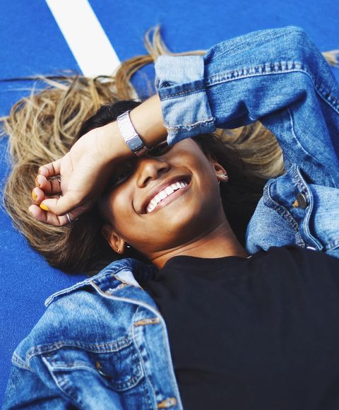 A girl laying on blue floor wearing a blue denim jacket, laughing. 