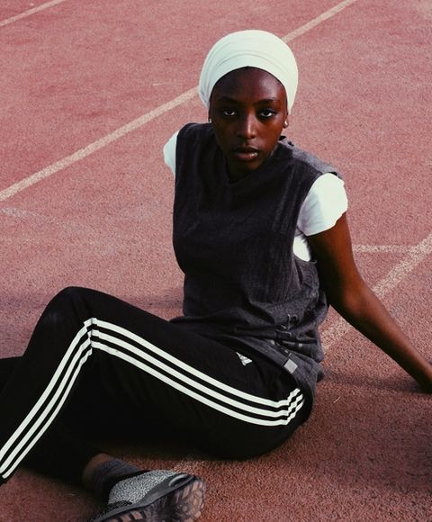 A woman in a green headscarf sitting on a running track looking at the camera 