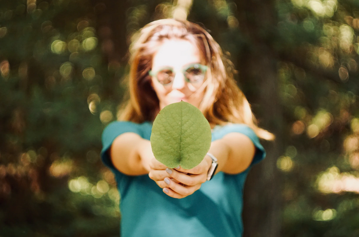 woman in green sunglasses holding a green leaf to the camera