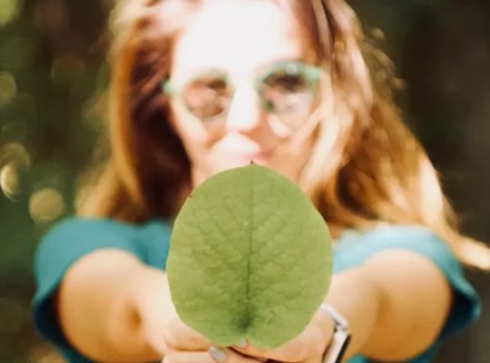 a women outside in the sun wearing glasses holding a leaf in front of her