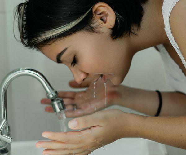 A girl leans over a sink with the tap running while washing her face 