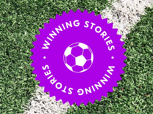 A big purple sticker with the words winning stories stamped on top of grass