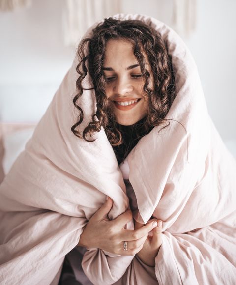 Una mujer sonriente envuelta en un edredón rosa, la máxima protección para el frío