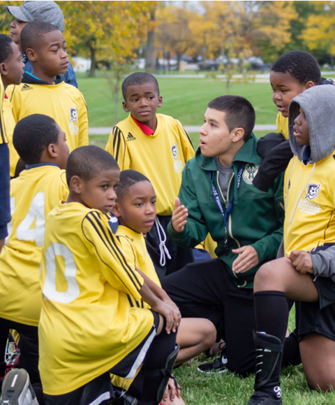 Entrenador de fútbol dando indicaciones a jóvenes jugadores.