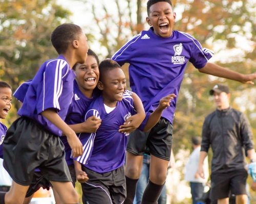 Cuatro chicos jovenes en uniformes de fútbol morados celebrando un gol