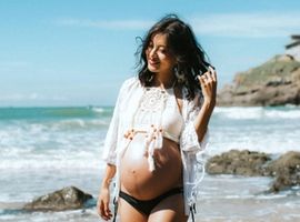 a pregnant lady walking along a sunny beach playing with her hair 
