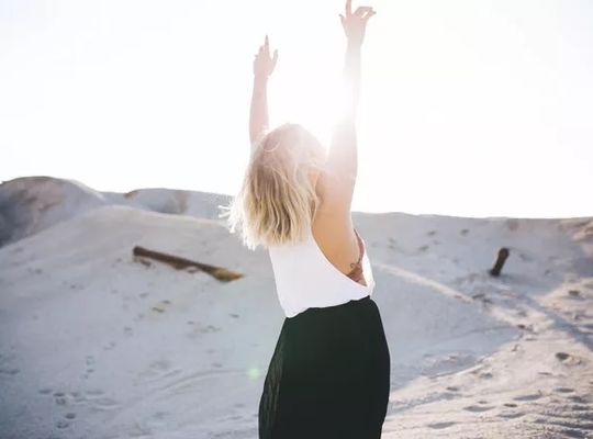 blonde woman on the beach stretching towards the sun