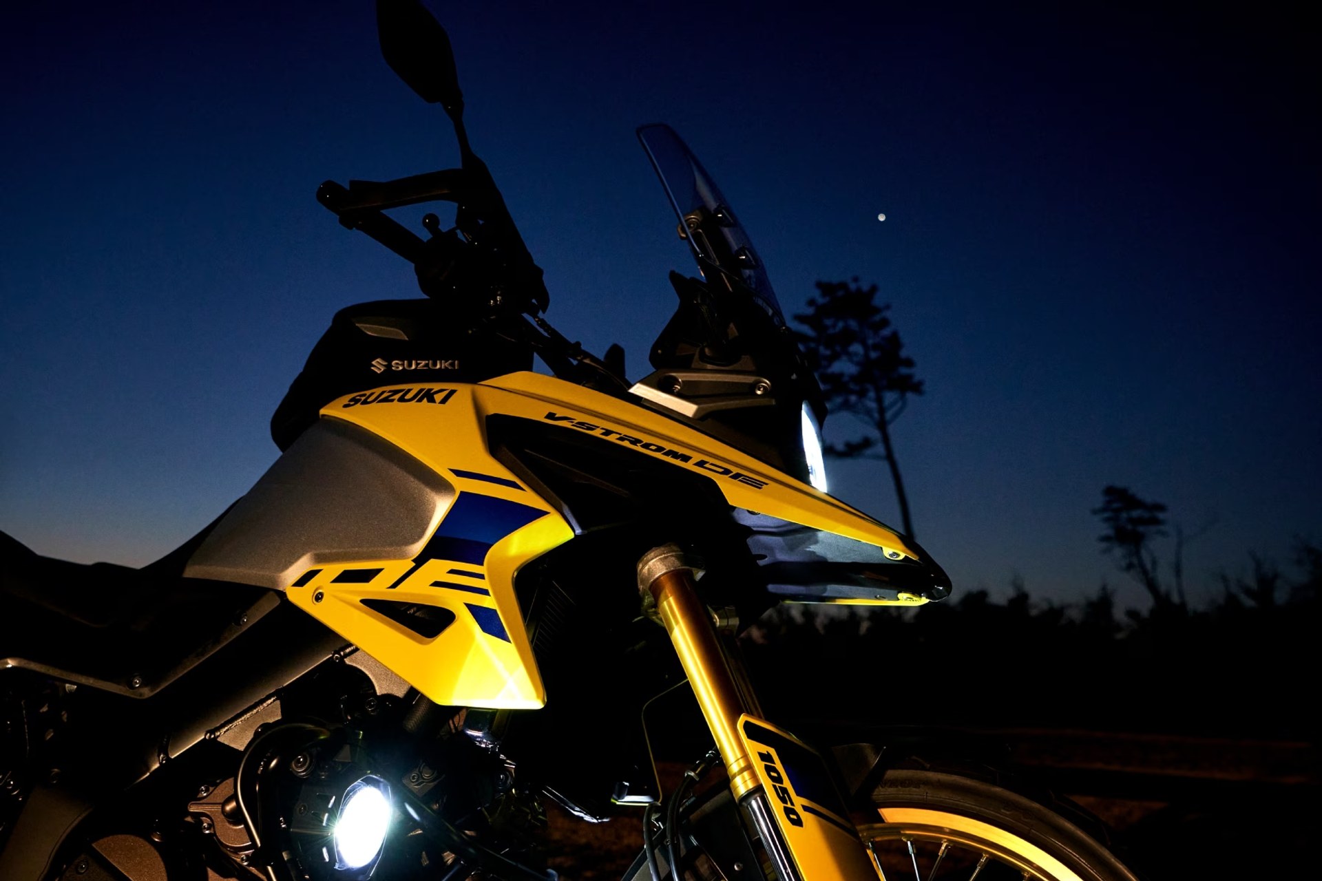 Motocicleta Suzuki V-Strom 1050DE amarilla de frente al atardecer