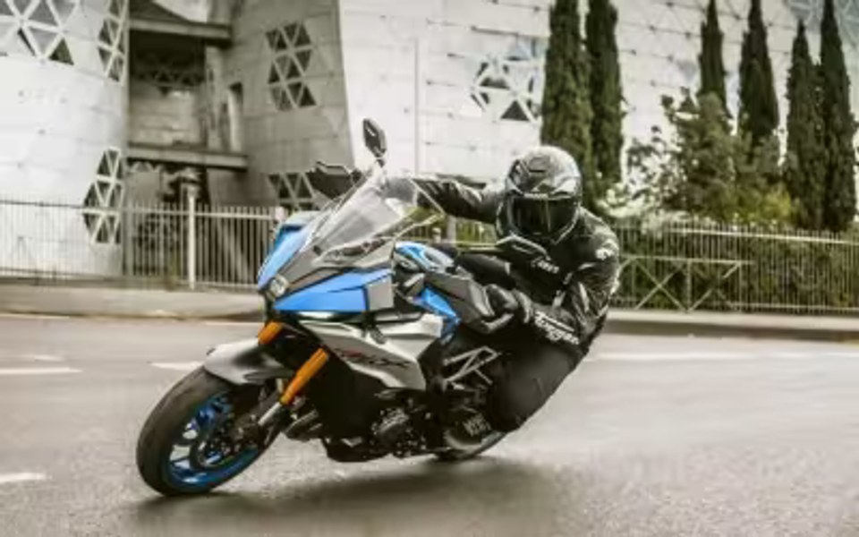 Piloto conduciendo una motocicleta Suzuki deportiva azul en una curva urbana