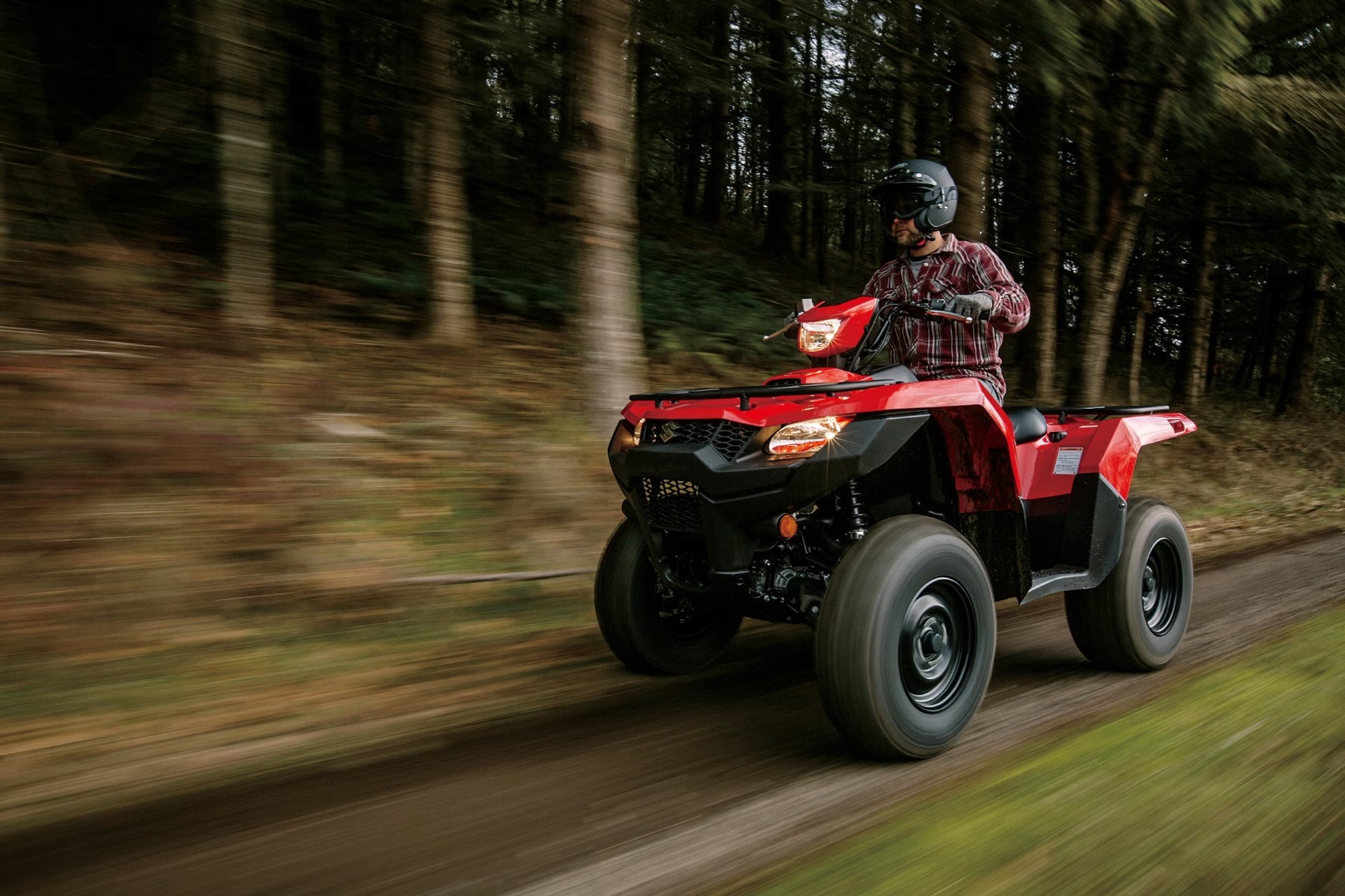 Conductor en Suzuki KingQuad 750 rojo recorriendo un camino de bosque