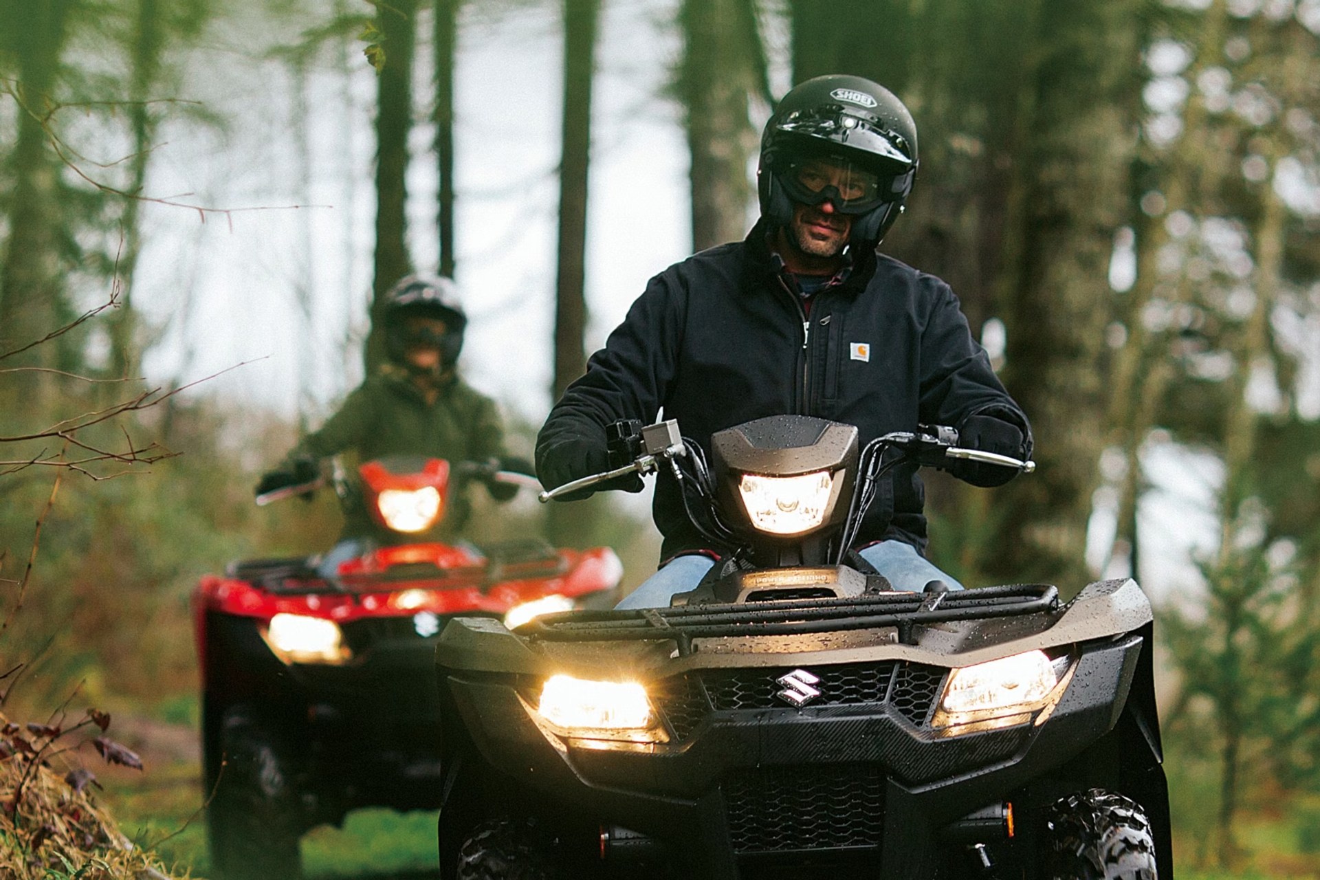 Dos conductores en Suzuki KingQuad 750 recorriendo un sendero de bosque