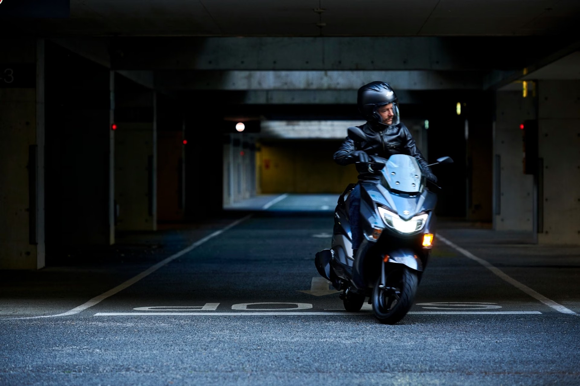 Piloto conduciendo un scooter Suzuki Burgman Street 125EX con faros LED encendidos en un estacionamiento subterráneo