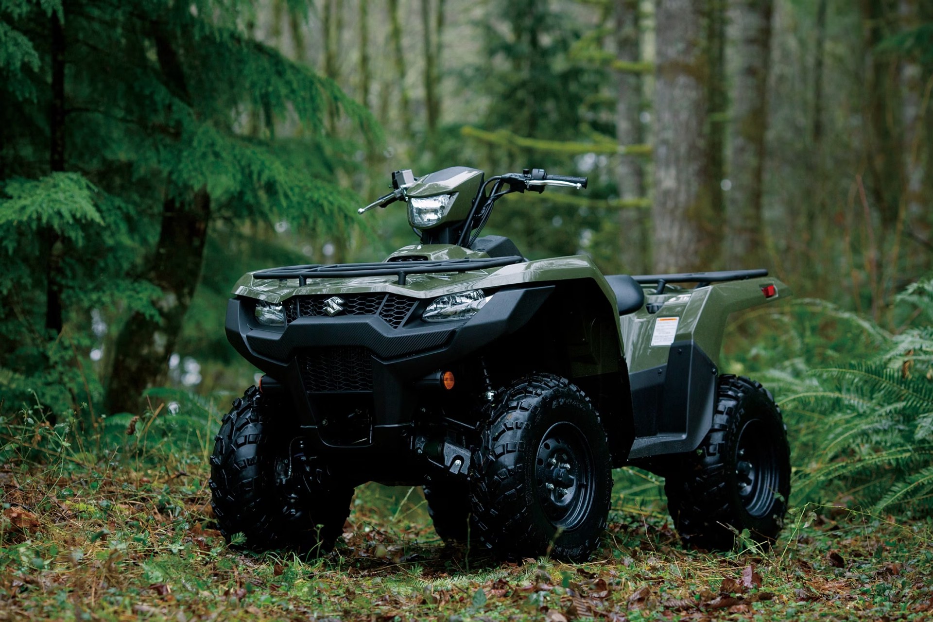 Suzuki KingQuad 750 verde estacionado en un entorno de bosque