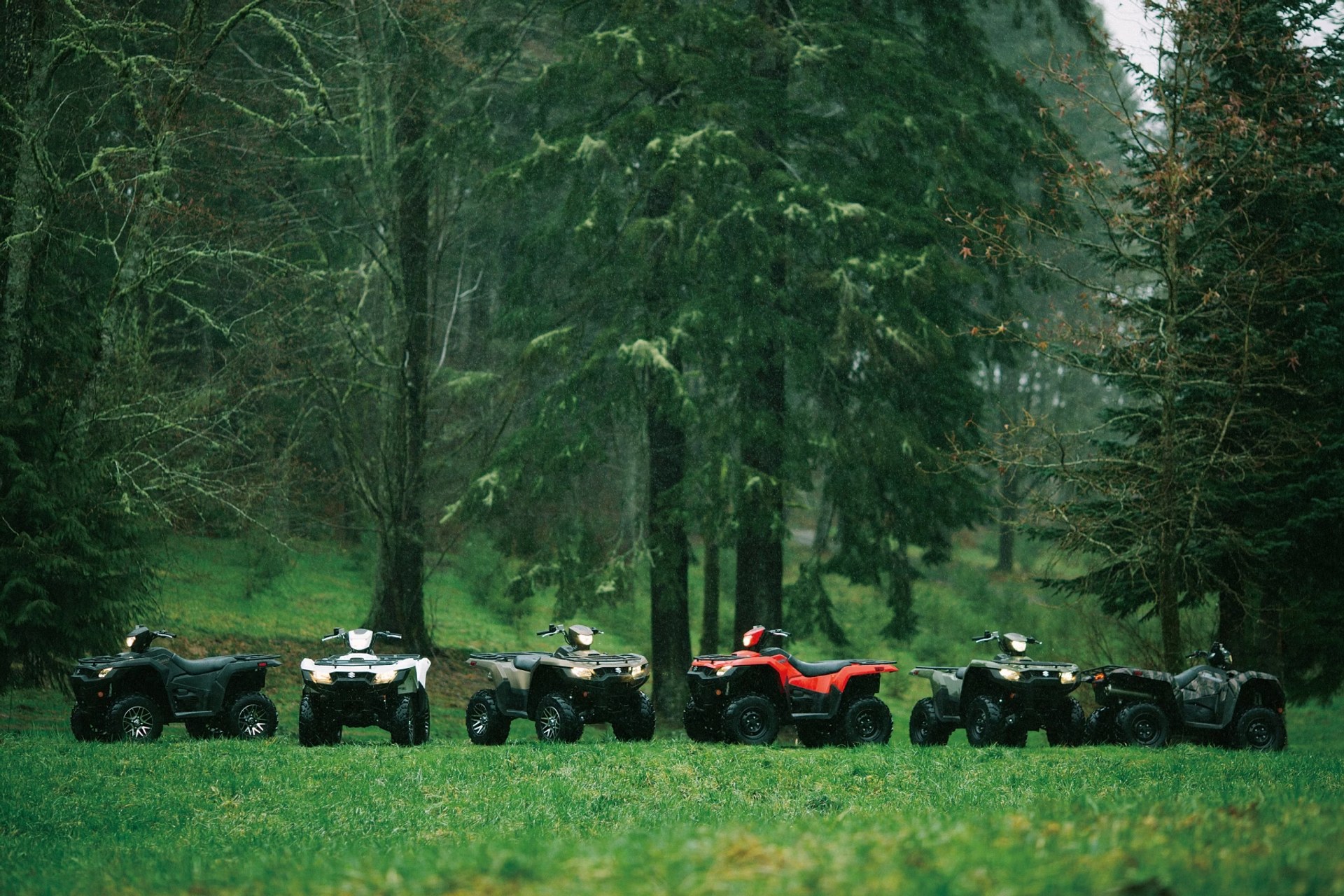 Cuatrimotos Suzuki KingQuad 750 de distintos colores estacionadas en un entorno de bosque