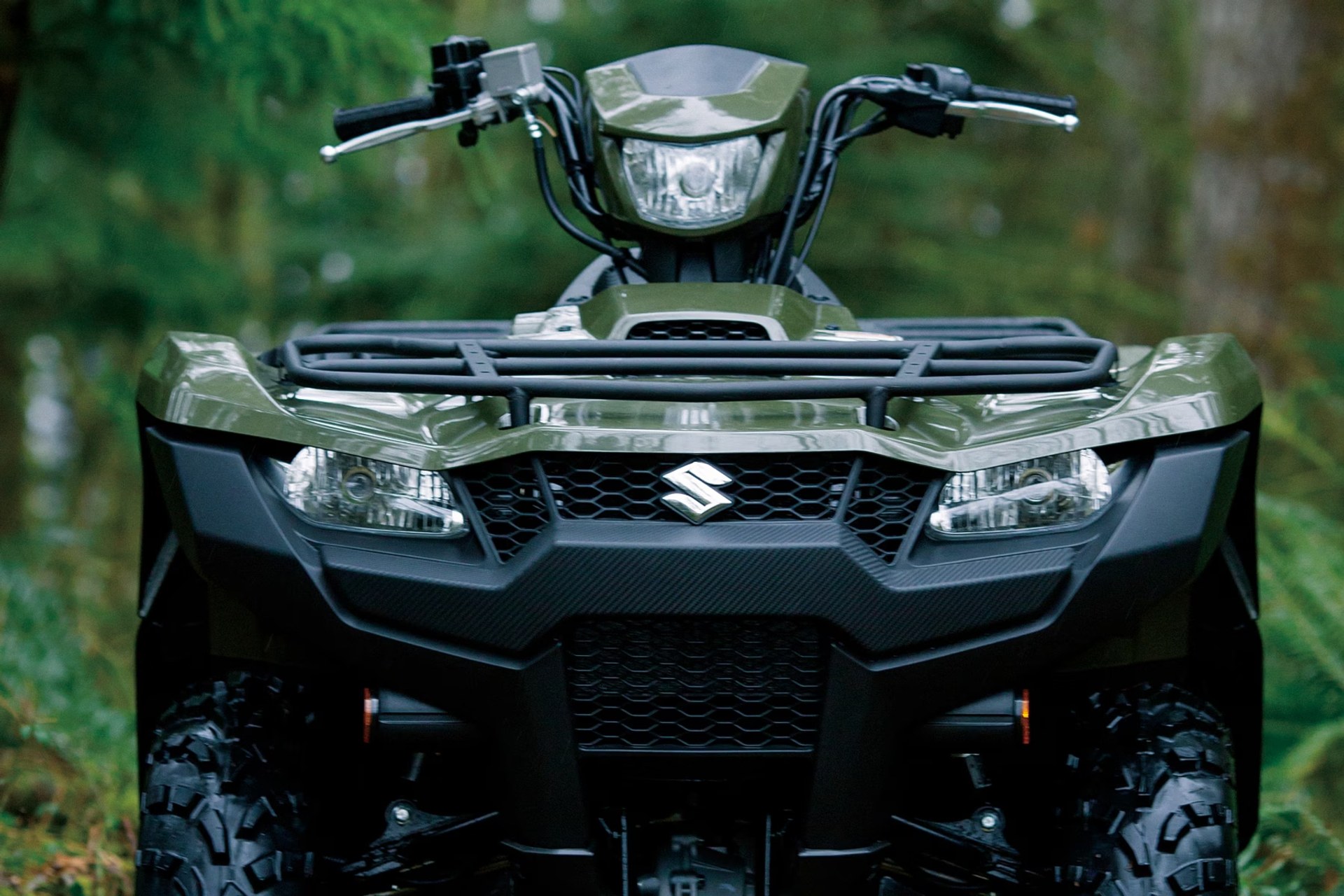Suzuki KingQuad 750 verde en vista frontal en un entorno de bosque