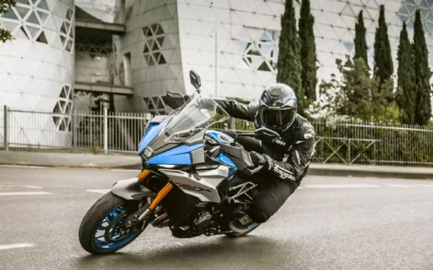 Piloto conduciendo una motocicleta Suzuki deportiva azul en una curva urbana
