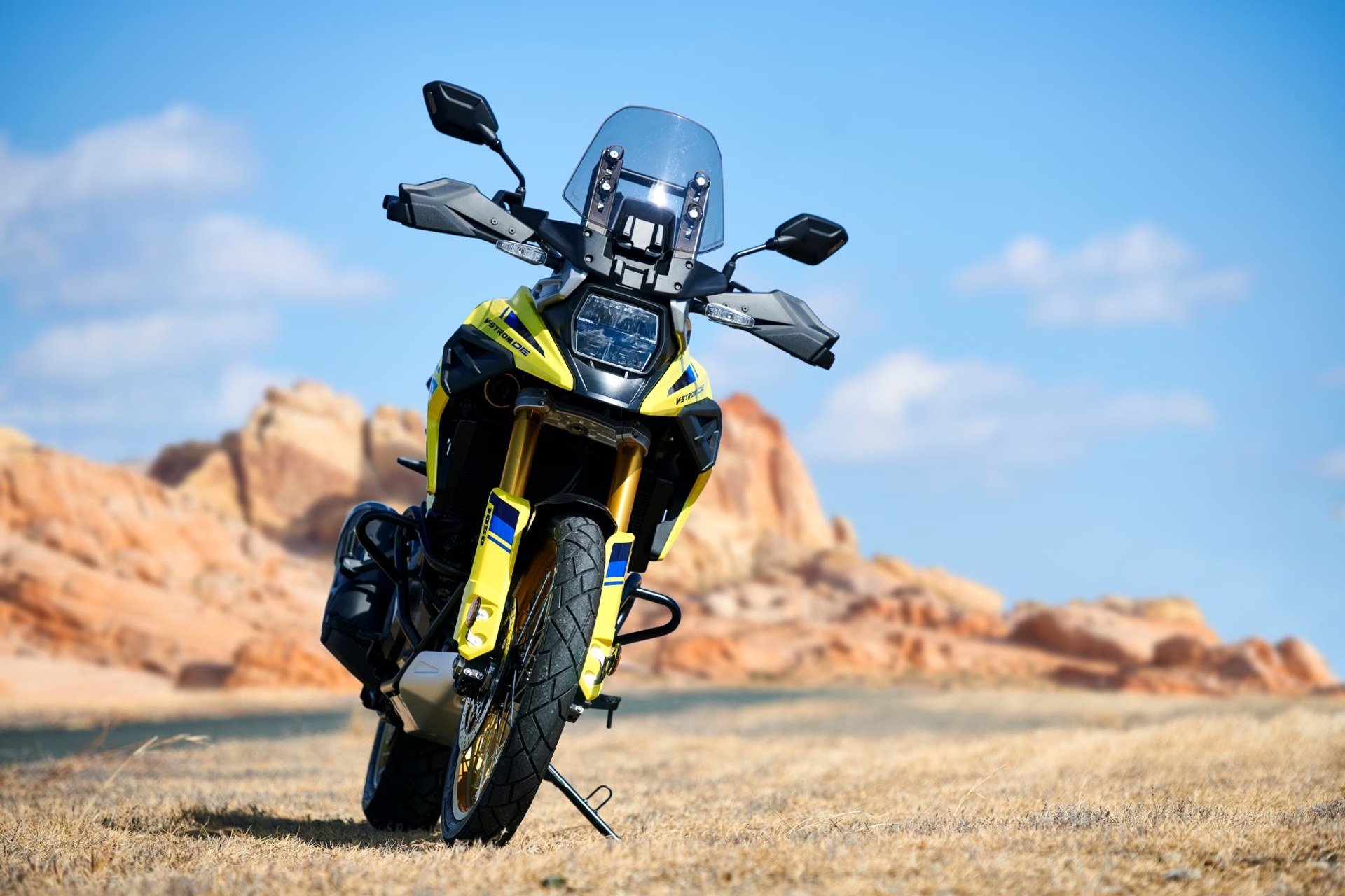 Motocicleta Suzuki V-Strom 1050DE amarilla vista de frente en un paisaje desértico rocoso