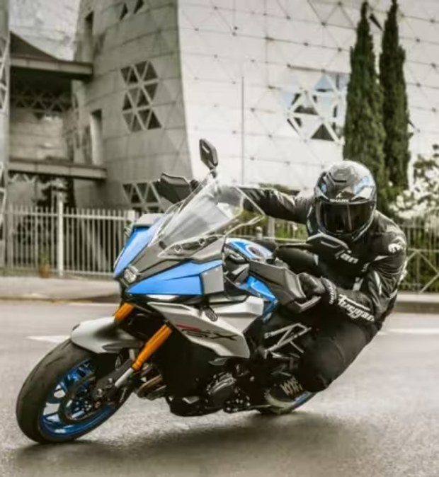 Piloto conduciendo una motocicleta Suzuki deportiva azul en una curva urbana