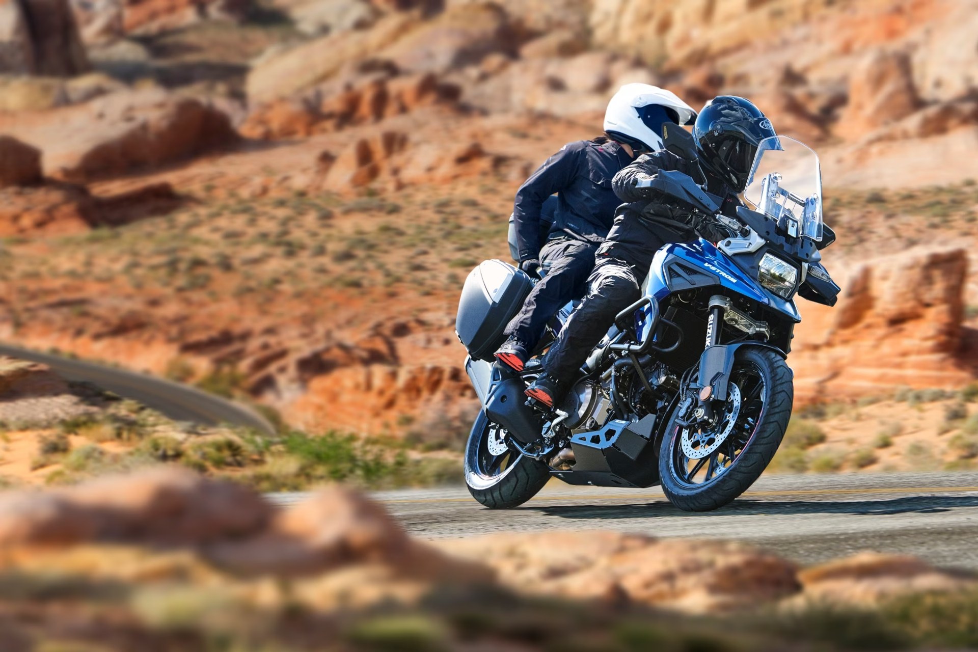 Dos motociclistas en Suzuki V-Strom 1050DE azul recorriendo una carretera de montaña