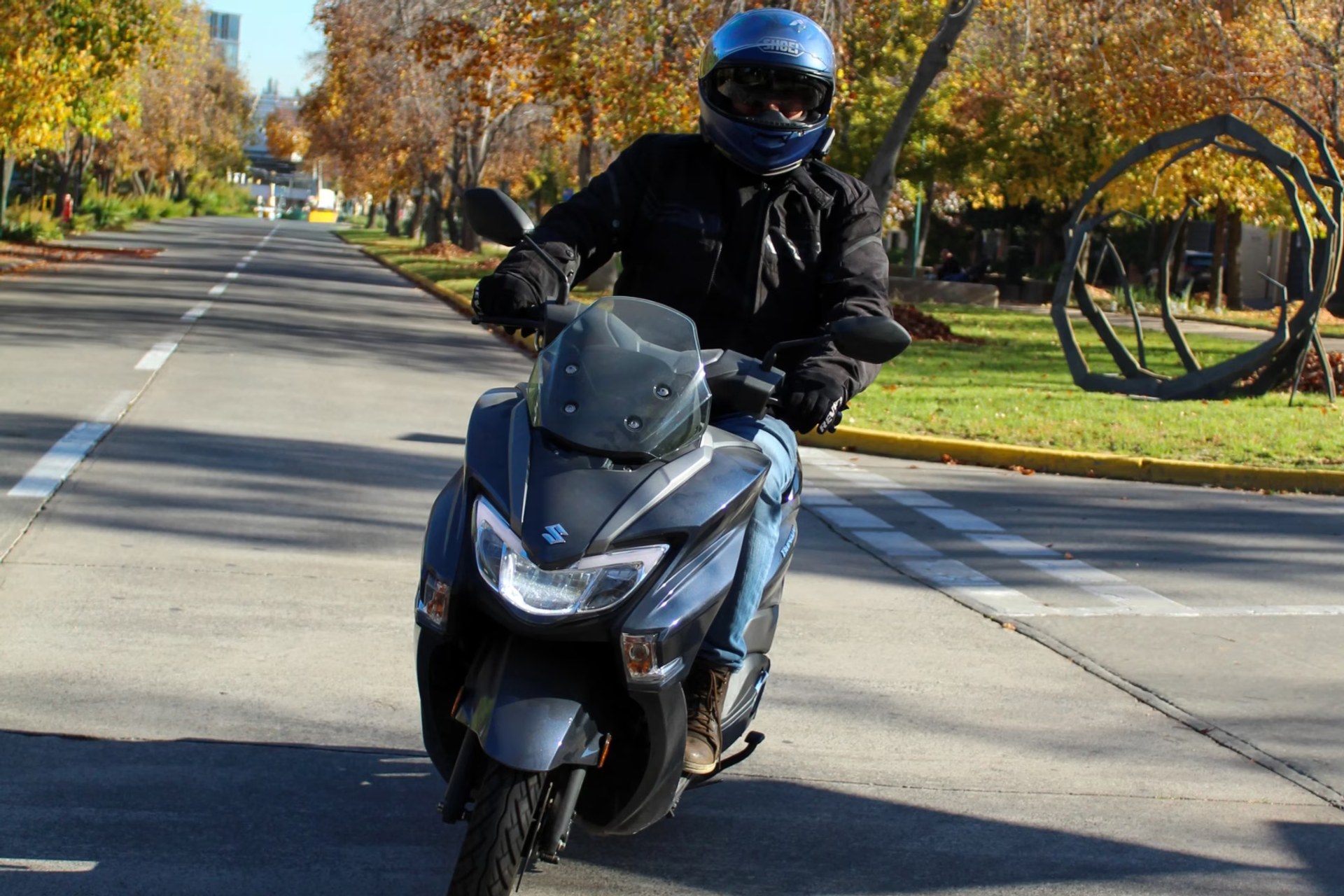 Piloto realizando un giro en curva con el scooter Suzuki Burgman Street 125EX en un entorno residencial arbolado