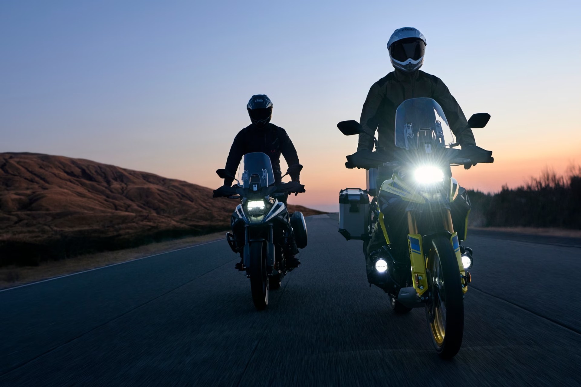 Dos motociclistas en Suzuki V-Strom 1050DE recorriendo una carretera al atardecer