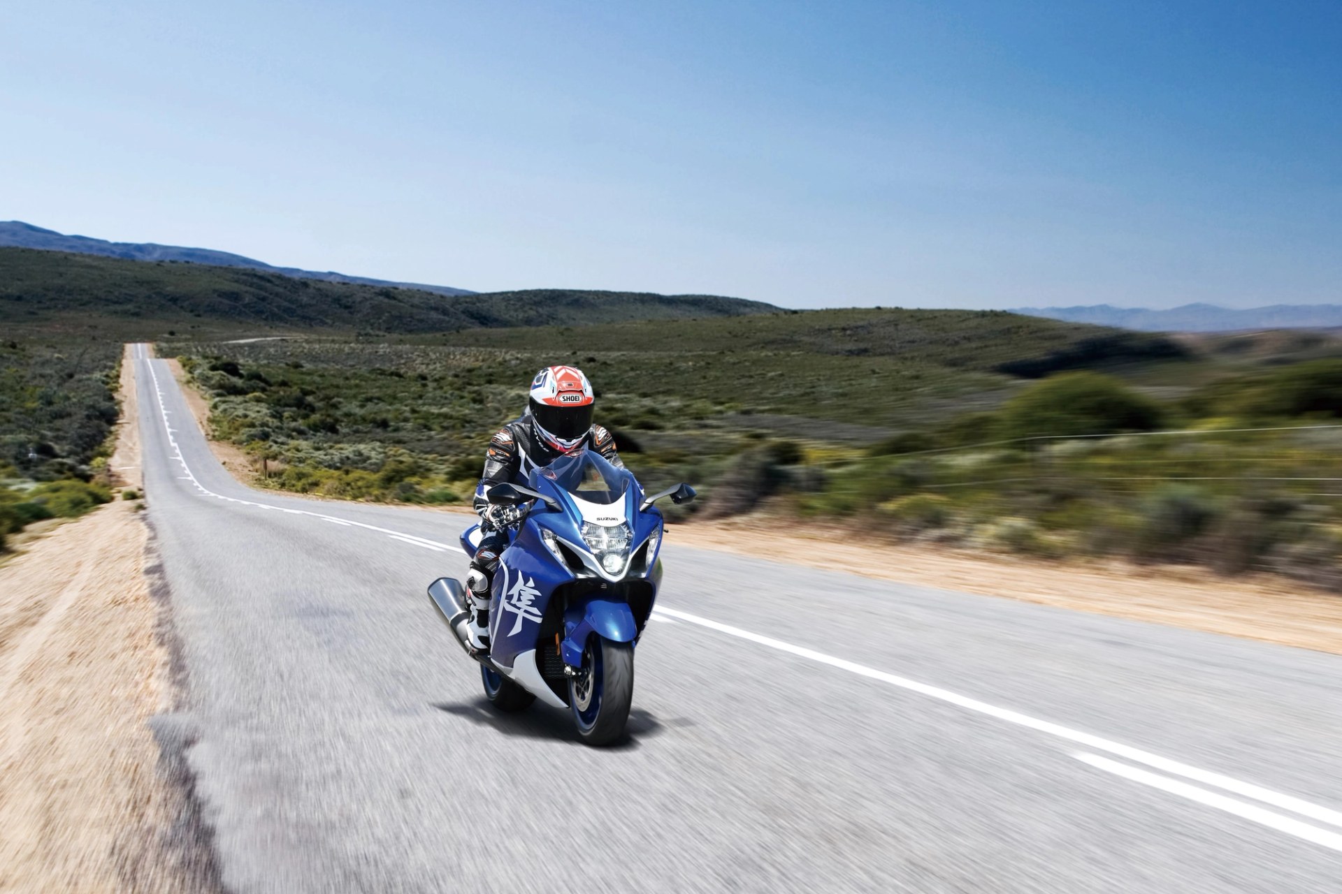 Piloto conduciendo una Suzuki Hayabusa azul en una carretera abierta rodeada de paisaje natural