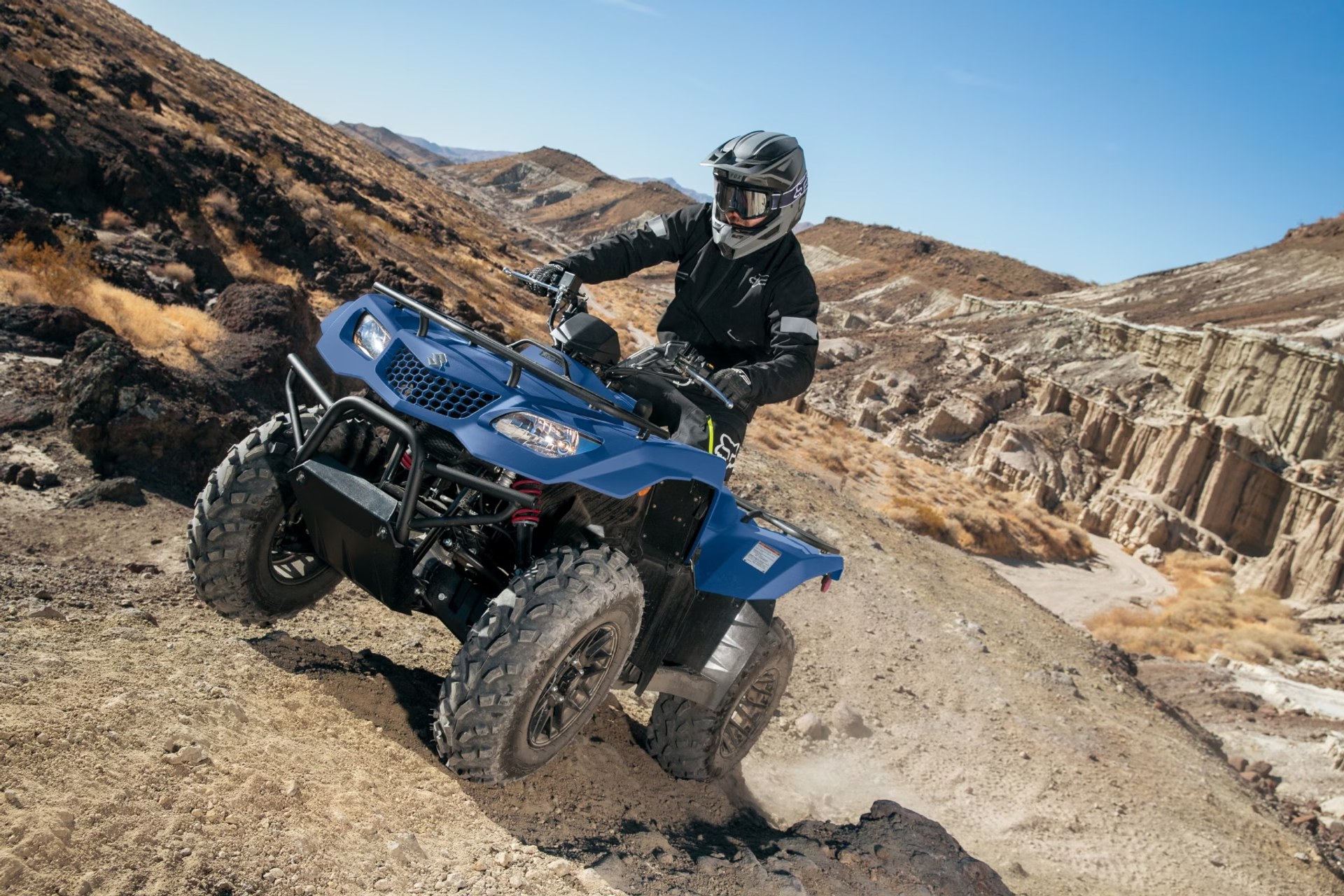 Motociclista conduciendo un Suzuki KingQuad 400 azul por terreno rocoso off-road