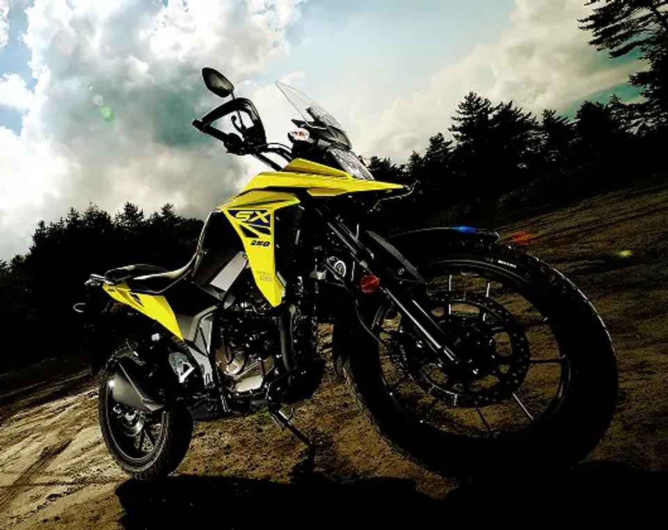 Motocicleta Suzuki V-Strom 250 amarilla en camino rural junto a paisaje boscoso