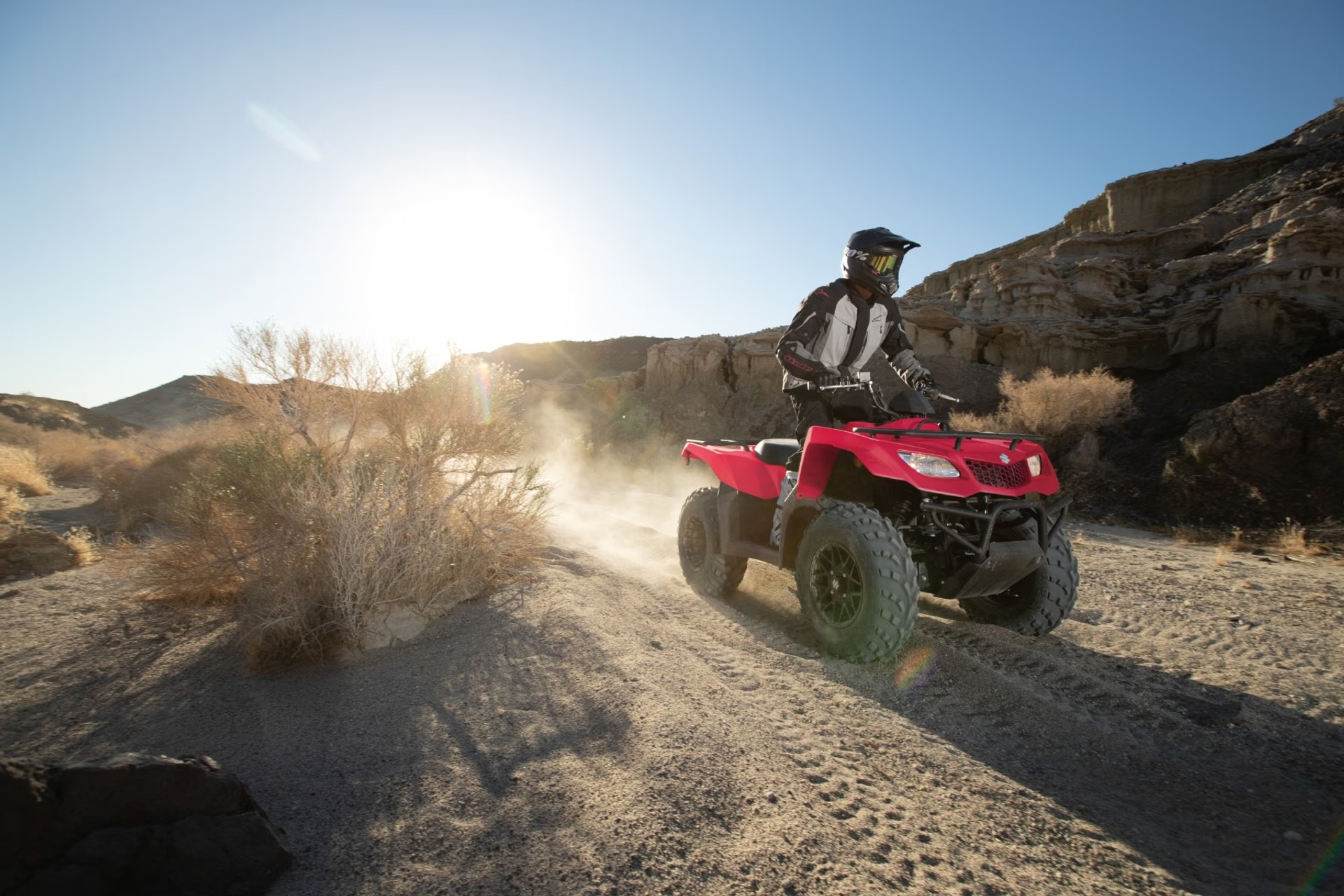 Motociclista conduciendo un Suzuki KingQuad 400 rojo por terreno desértico off-road