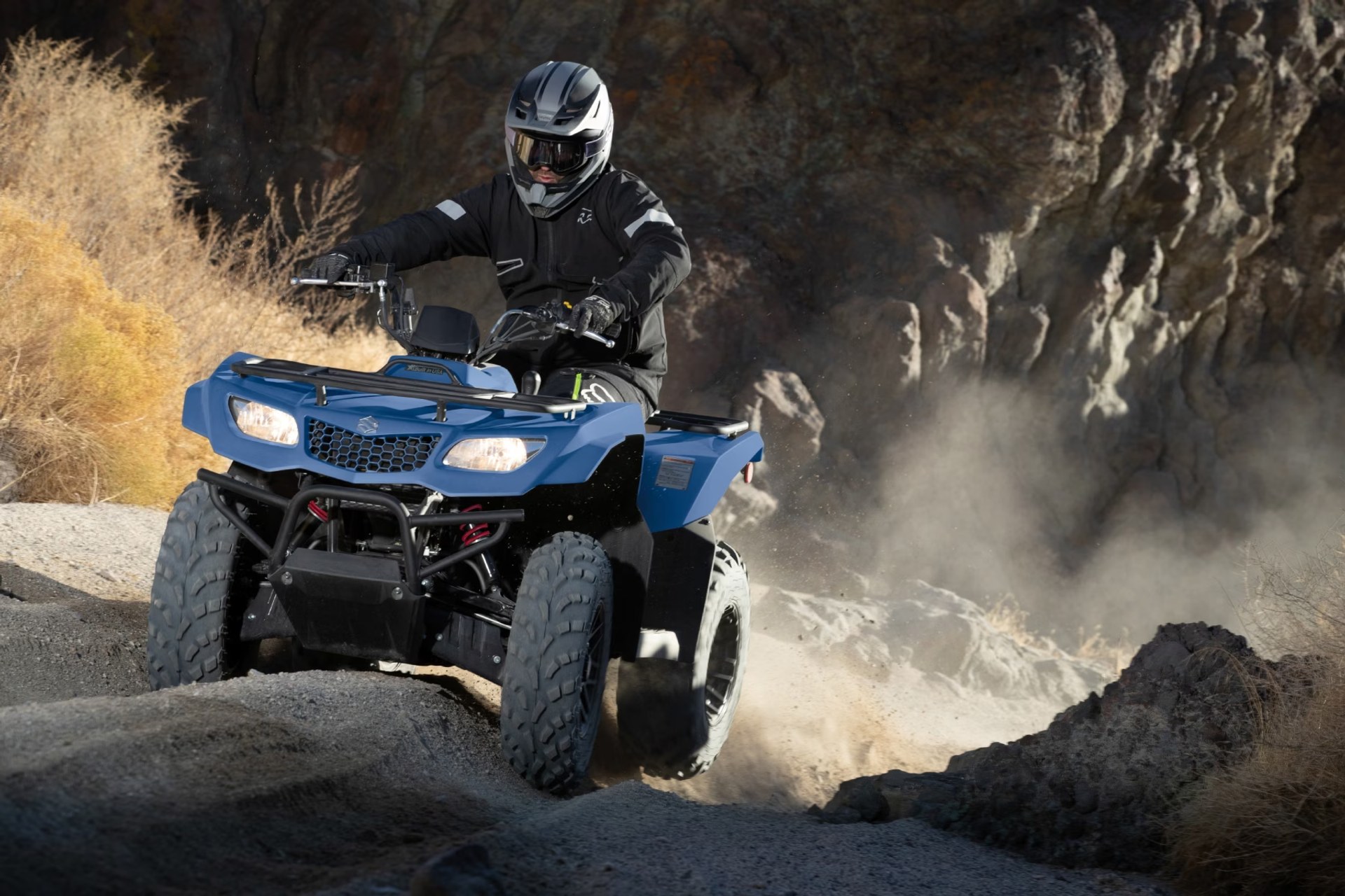 Conductor en Suzuki KingQuad 400 azul recorriendo terreno rocoso off-road