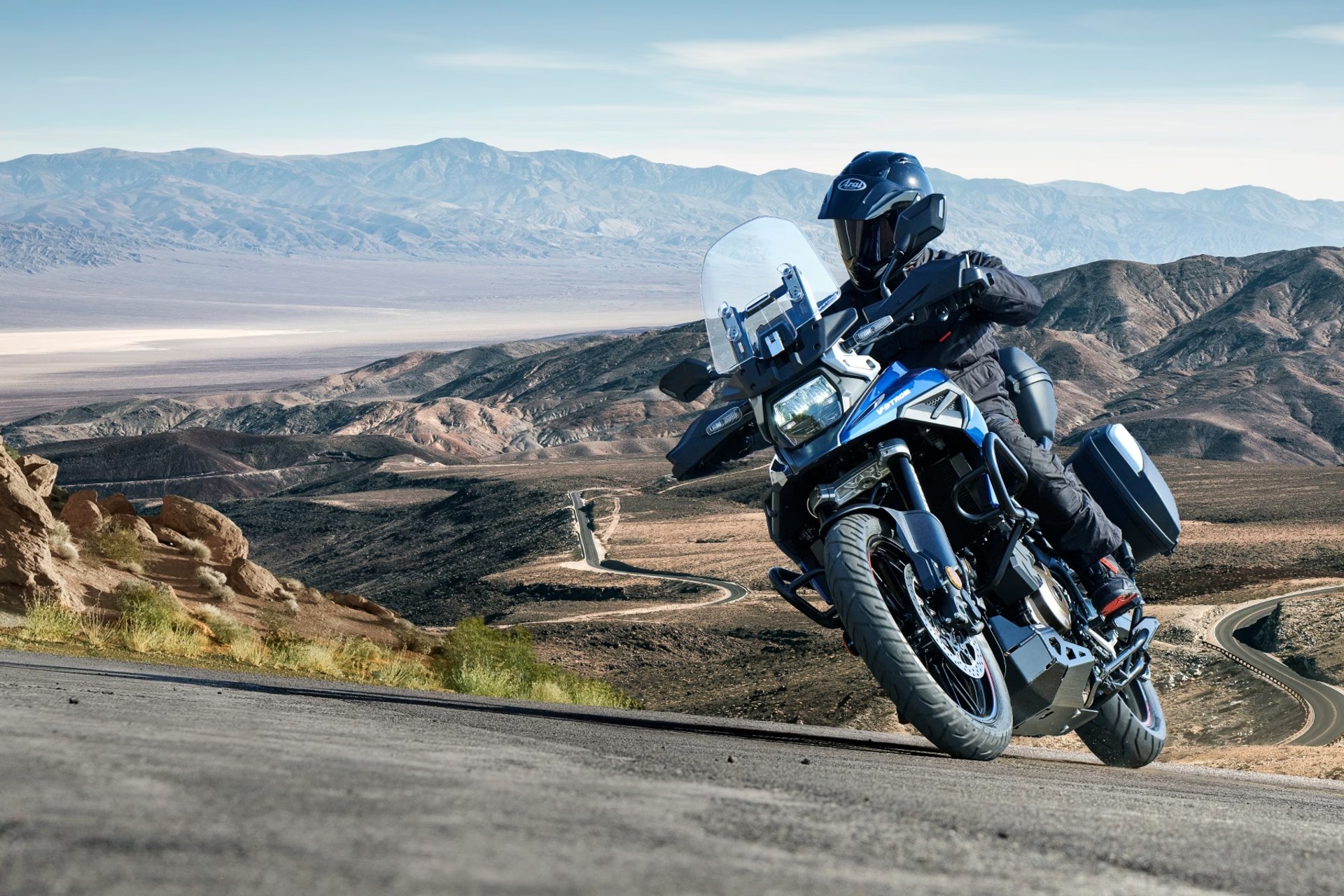 Motociclista en Suzuki V-Strom 1050DE azul recorriendo una carretera de montaña