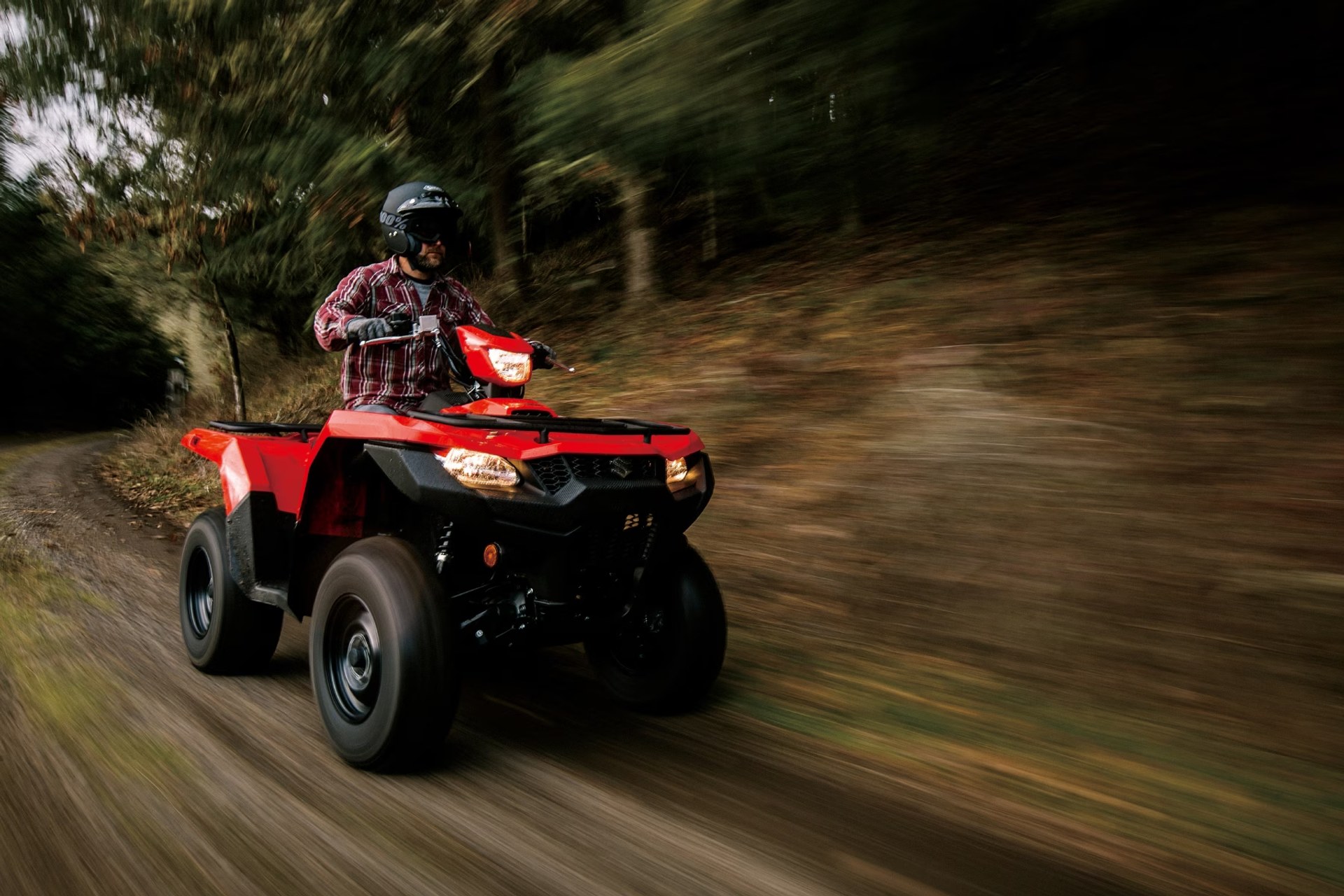 Conductor en Suzuki KingQuad 750 rojo recorriendo un sendero de bosque