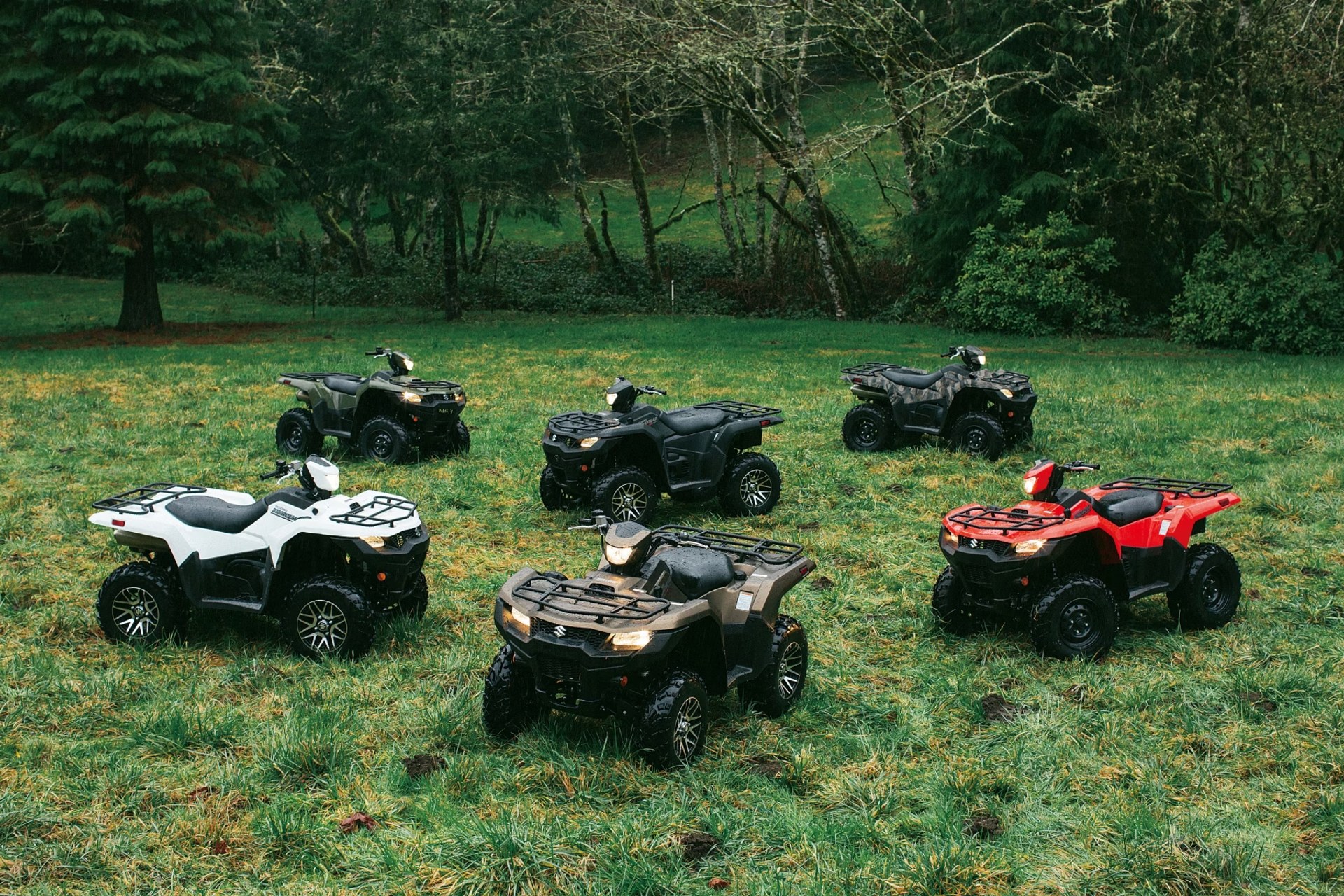 Cuatrimotos Suzuki KingQuad 750 de distintos colores estacionadas en un entorno de bosque