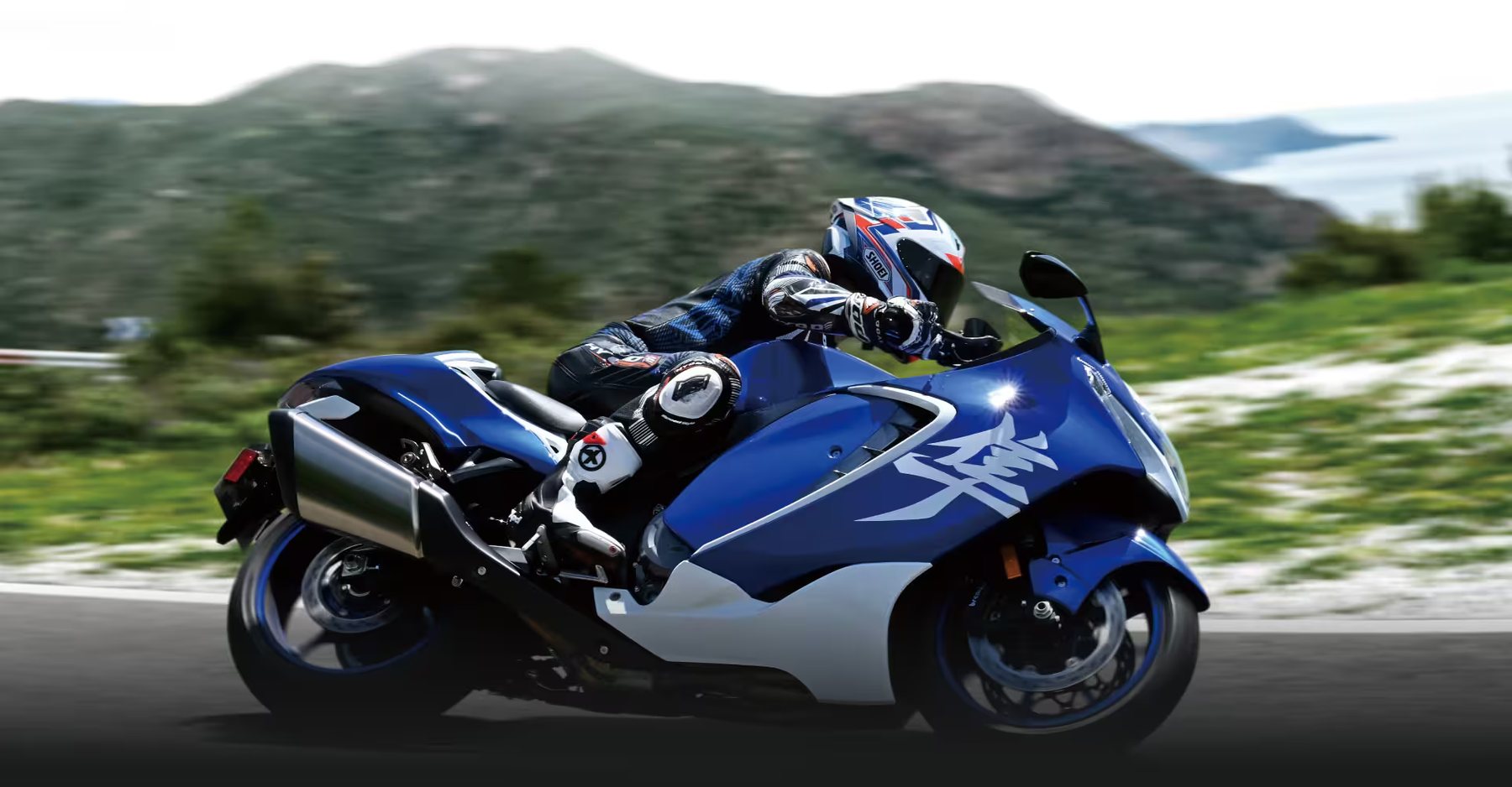 Piloto conduciendo una motocicleta Suzuki Hayabusa azul en carretera de montaña