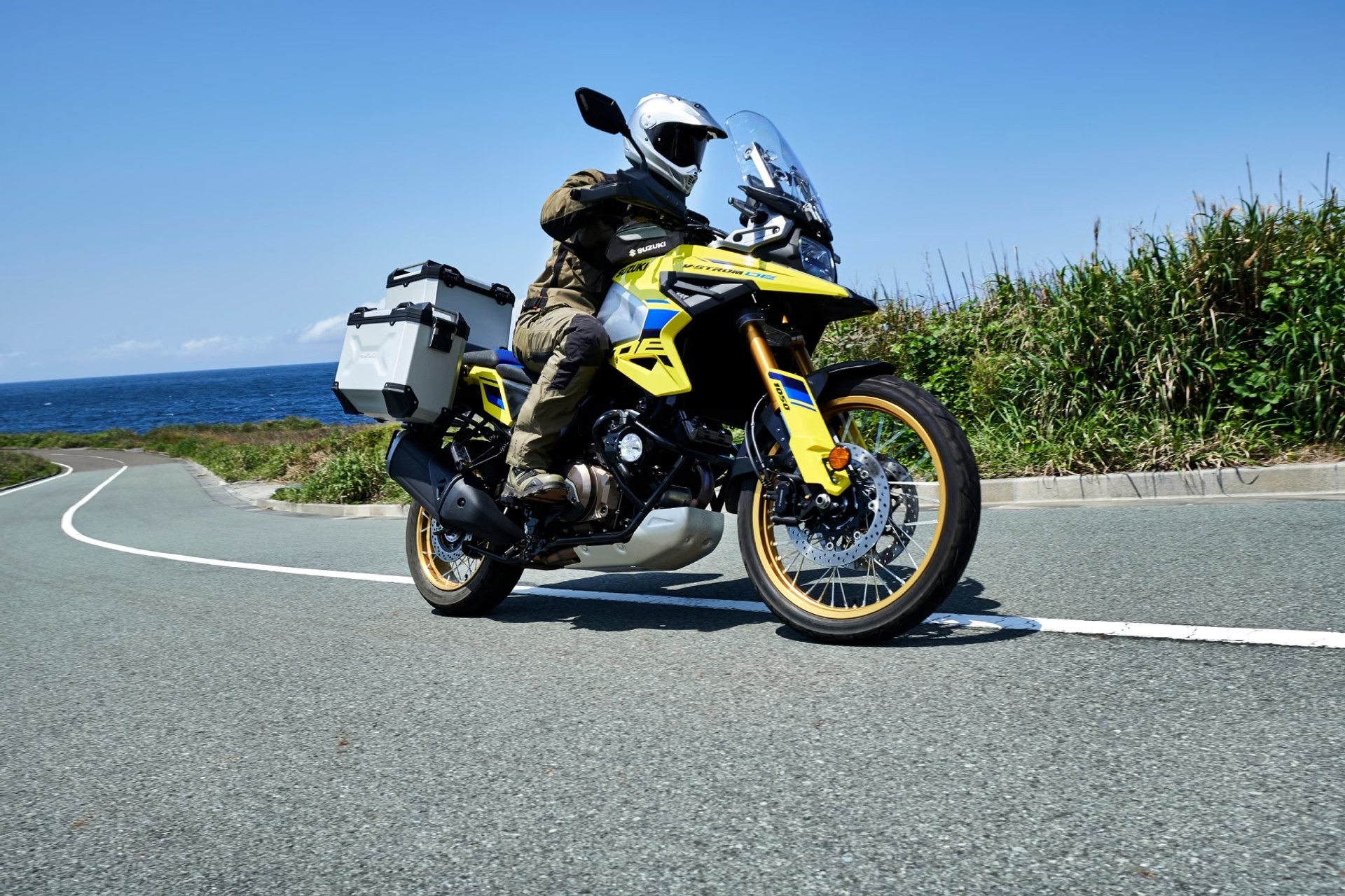 Motociclista en Suzuki V-Strom 1050DE amarilla recorriendo una carretera costera