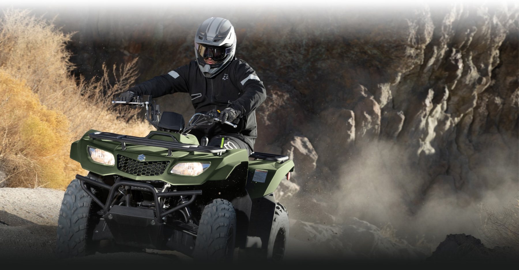 Cuatrimoto Suzuki verde conducida por motociclista en terreno rocoso