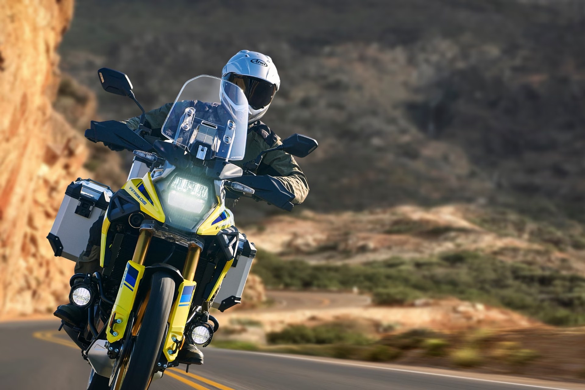Motociclista en Suzuki V-Strom 1050DE amarilla recorriendo una carretera de montaña