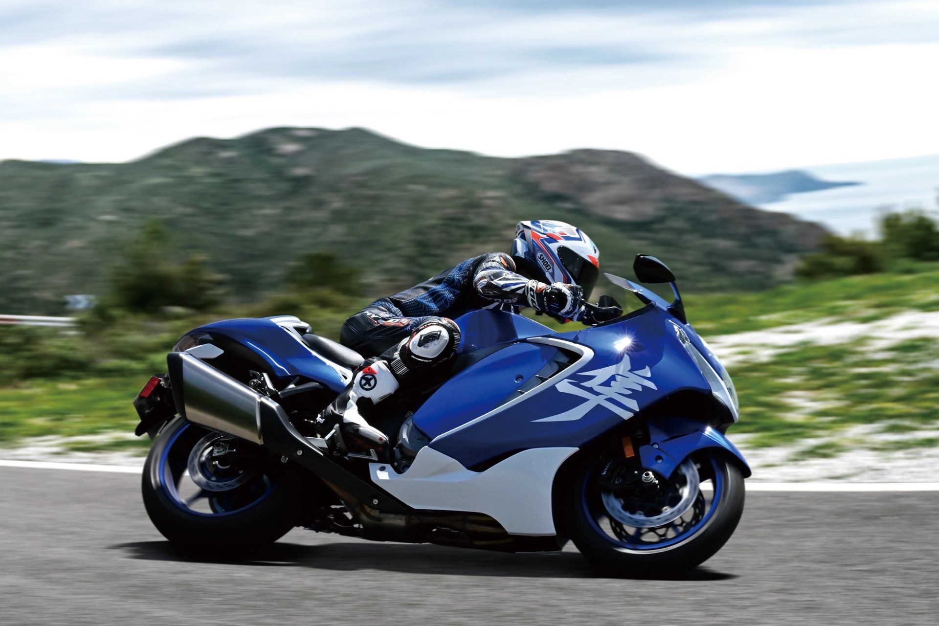Piloto conduciendo una Suzuki Hayabusa azul en carretera con paisaje montañoso