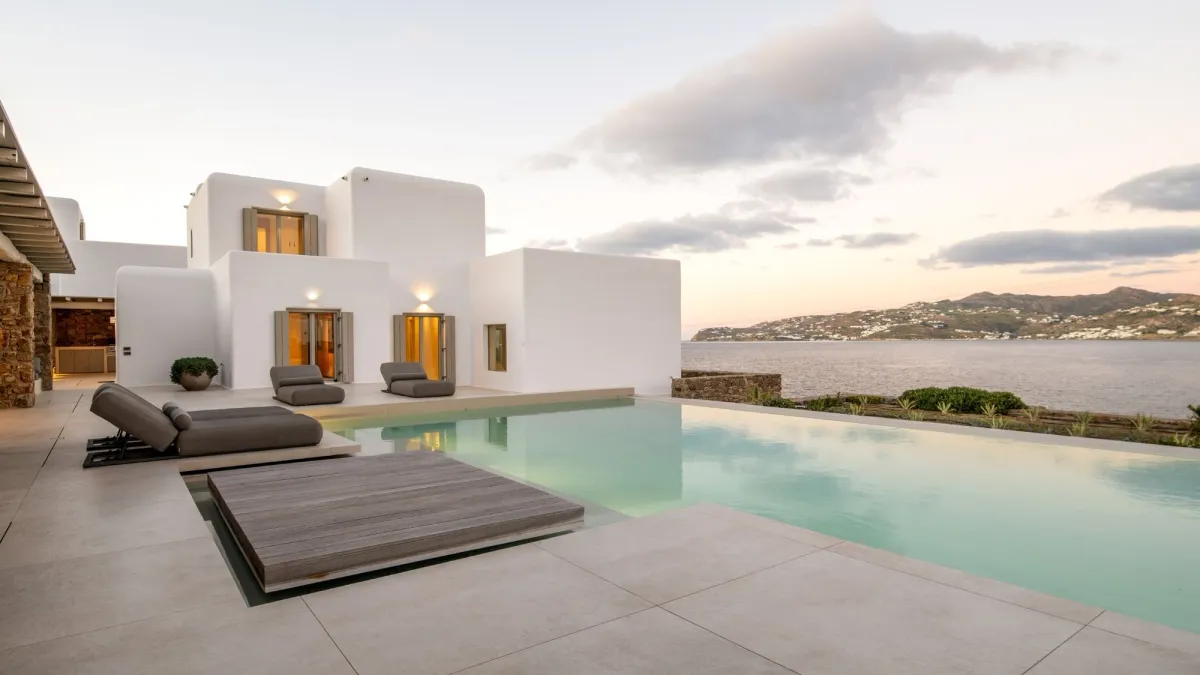 Luxury whitewashed villa in Mykonos with an infinity pool, sea views and minimalist outdoor lounge areas at sunset.