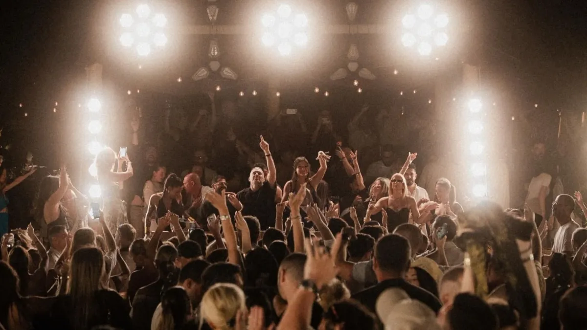 Crowded Mykonos nightlife event with guests dancing under bright stage lights at a packed evening venue.