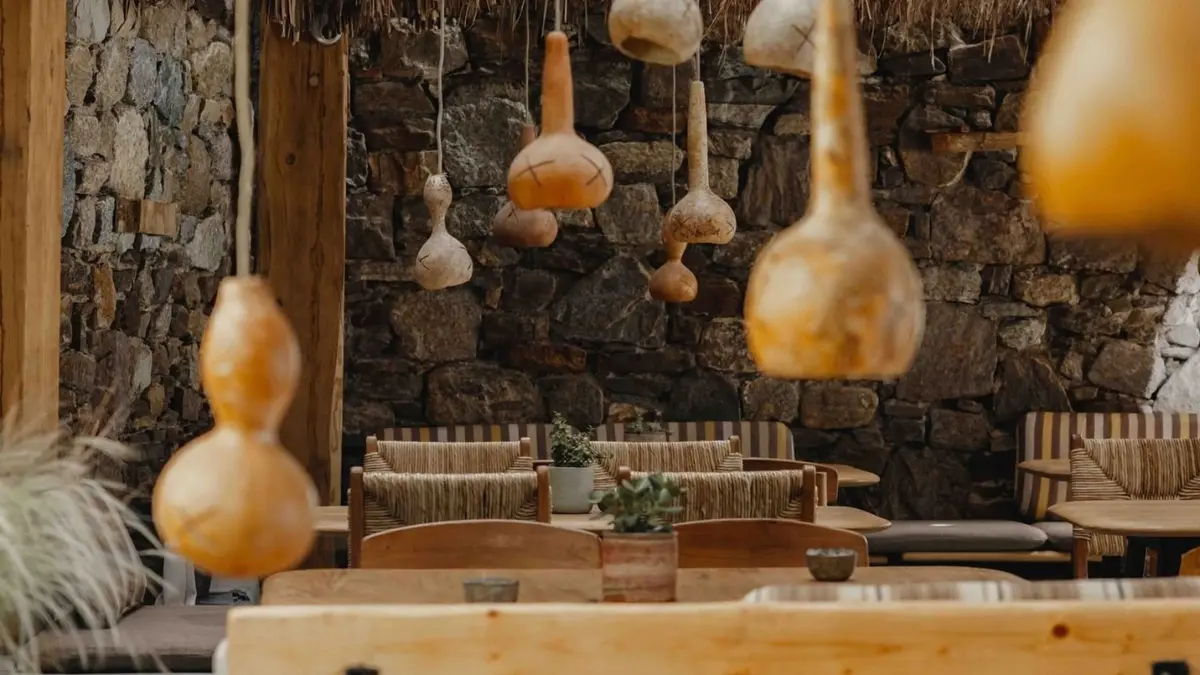 Relaxed Mykonos restaurant interior with natural wood furnishings, stone walls and handcrafted hanging décor, creating a warm and peaceful dining atmosphere.