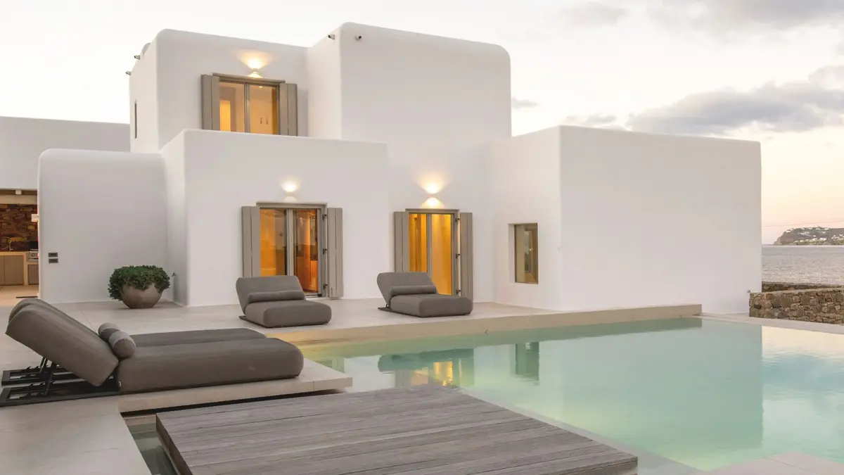 Luxury white Mykonos villa with a private infinity pool, outdoor loungers and sea views at sunset.