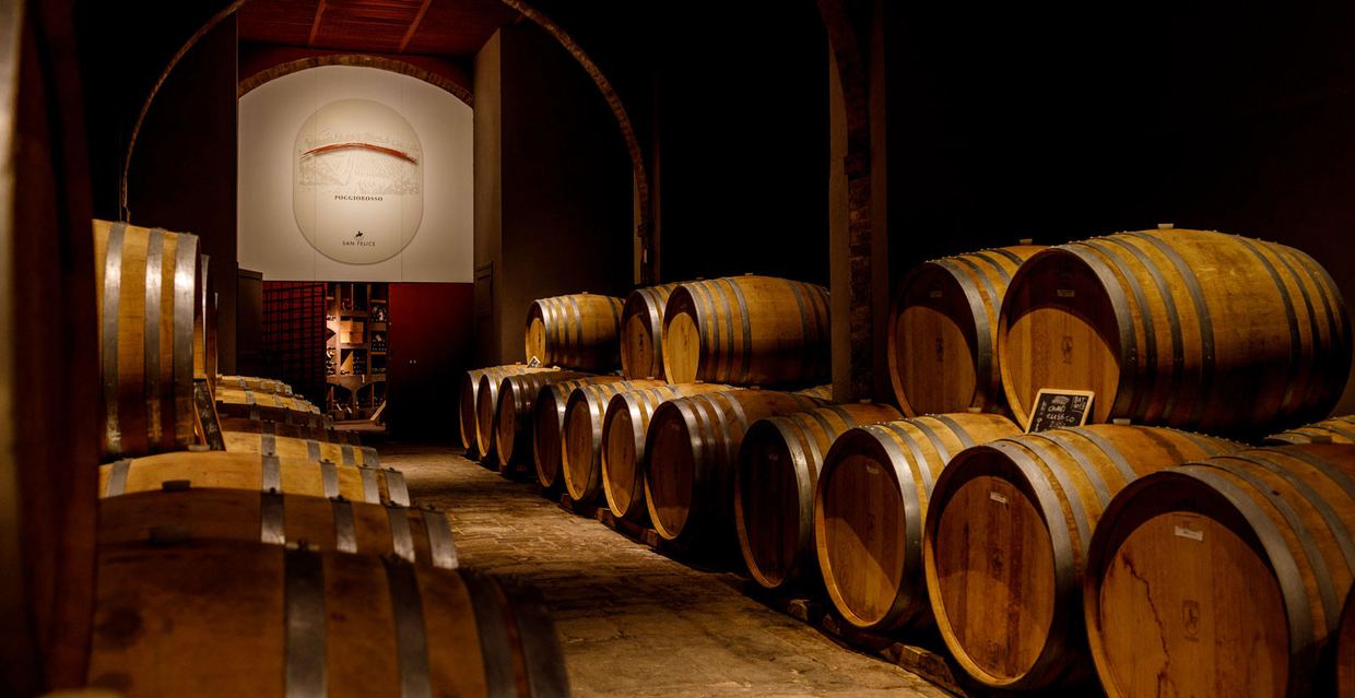 The barrel cellar at San Felice: rows of oak barriques beneath brick arches, with the Poggio Rosso emblem on the far wall
