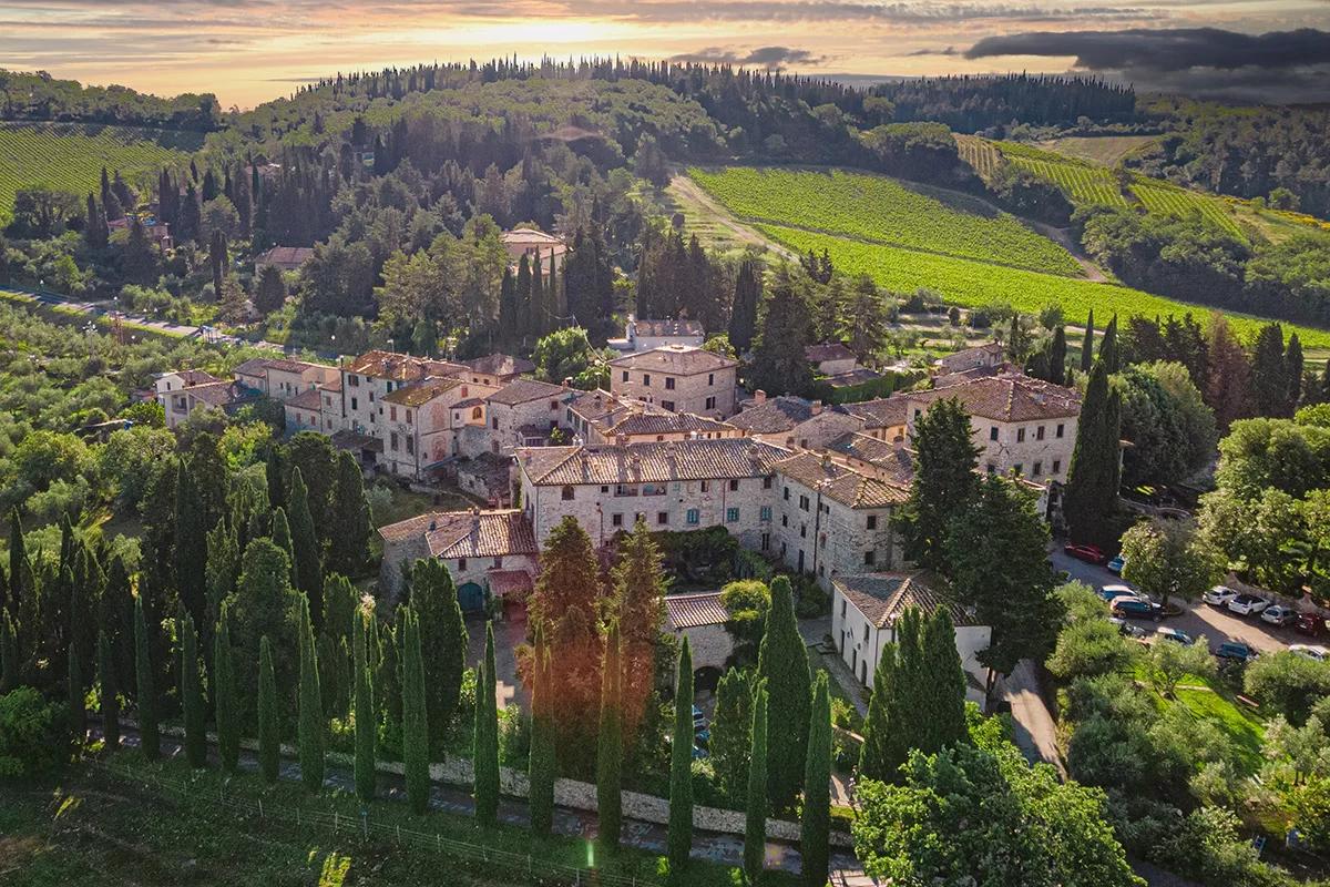 Aerial view of the hamlet of Fonterutoli at sunset: stone houses among cypresses, with the Mazzei vineyards on the hills behind