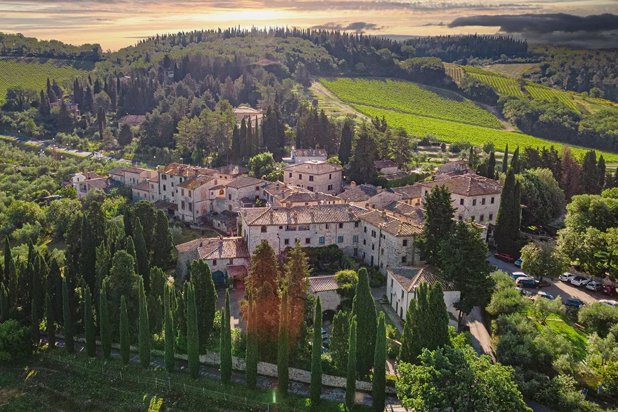 Aerial view of the hamlet of Fonterutoli at sunset: stone houses among cypresses, with the Mazzei vineyards on the hills behind